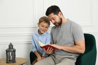 Photo of Muslim man and his son reading Quran at home