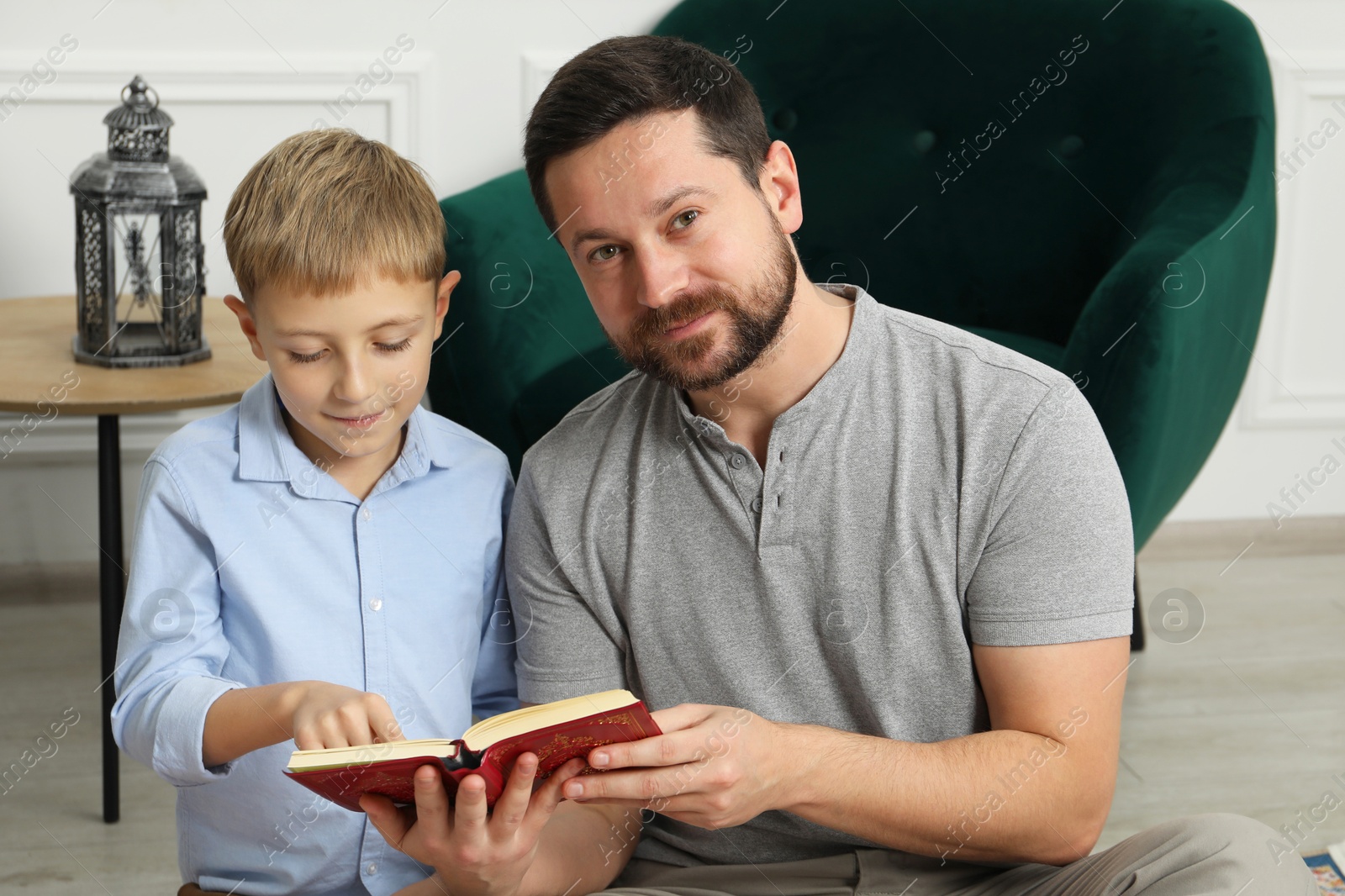 Photo of Muslim man and his son reading Quran at home