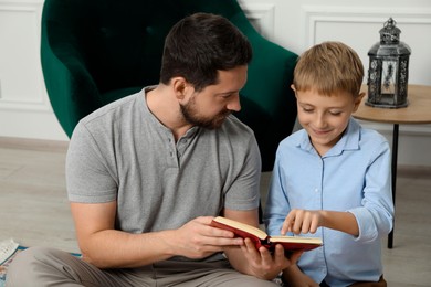 Photo of Muslim man and his son reading Quran at home