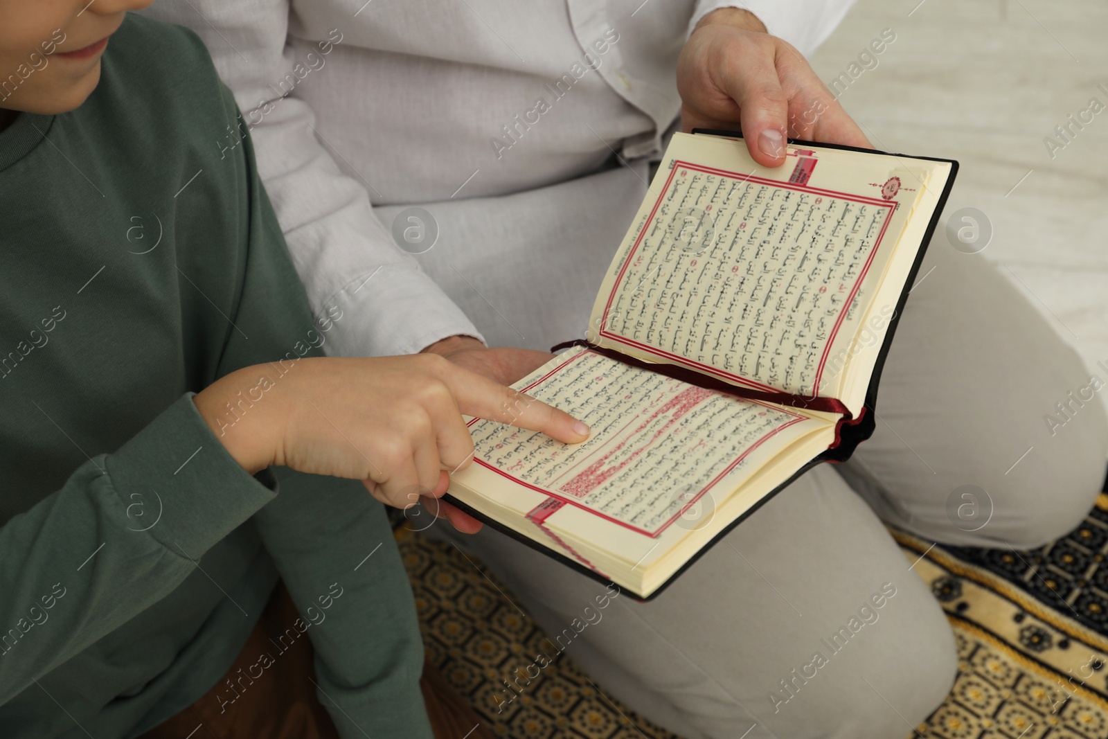 Photo of Muslim man and his son reading Quran at home, closeup