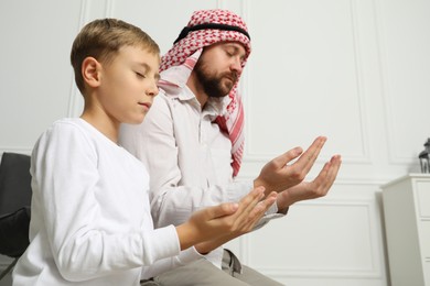 Photo of Muslim man and his son with beads praying indoors, low angle view