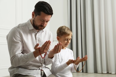 Photo of Muslim man and his son with beads praying indoors