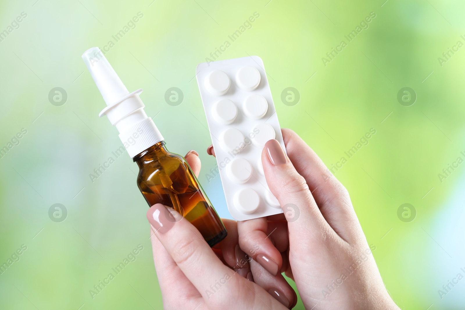 Photo of Allergy treatment. Woman with nasal spray and pills on blurred background, closeup