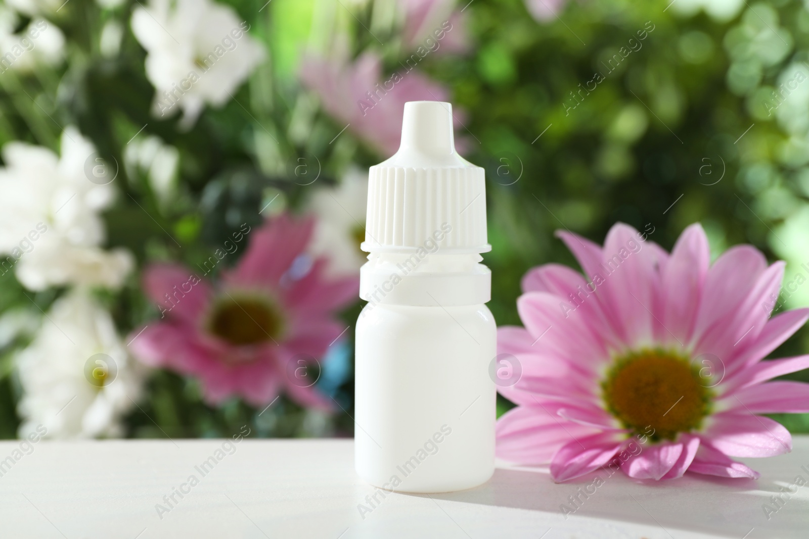 Photo of Allergy treatment. Bottle of medical drops and flower on white table against blurred background, closeup