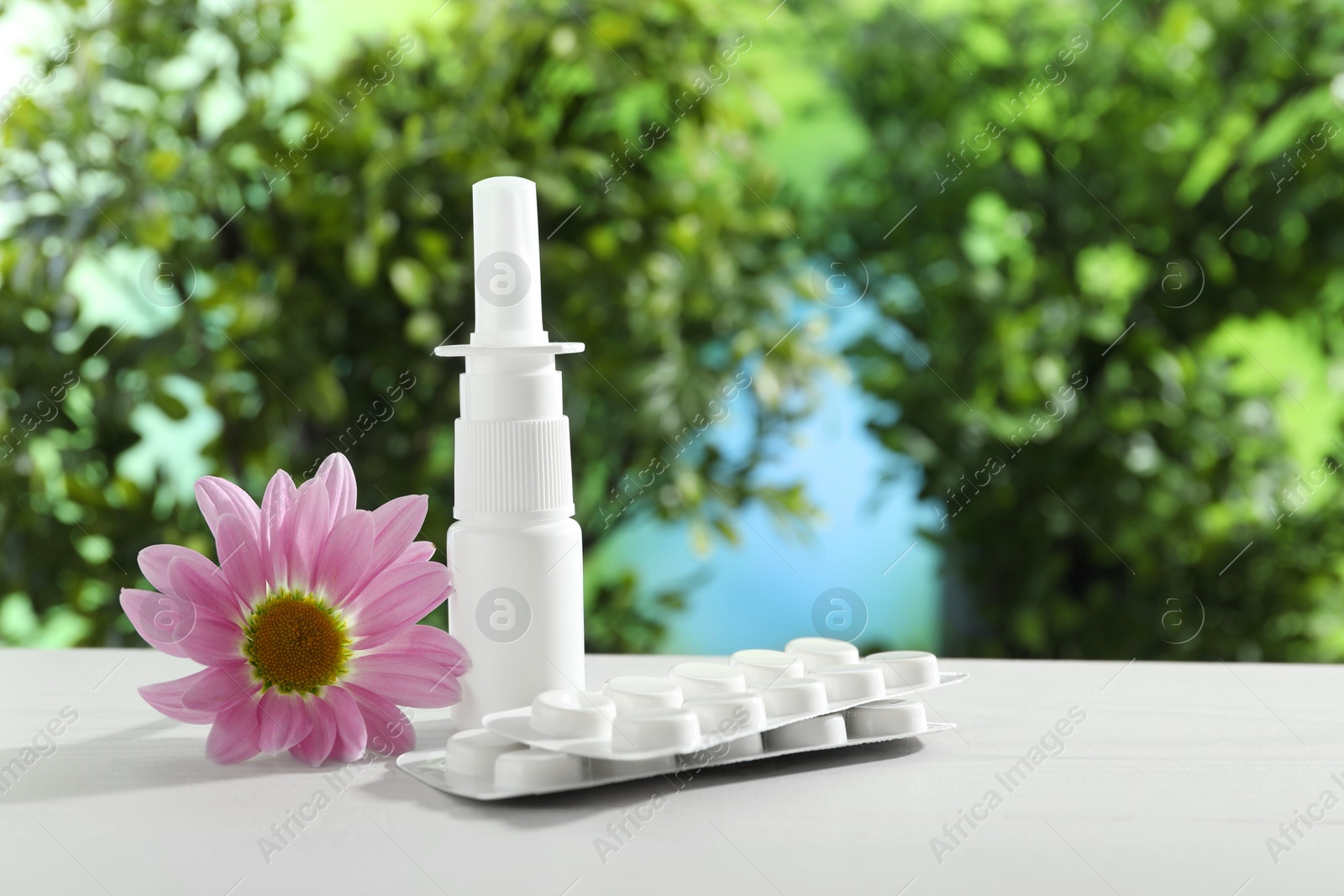 Photo of Allergy treatment. Nasal spray, pills and flower on white table against blurred background. Space for text