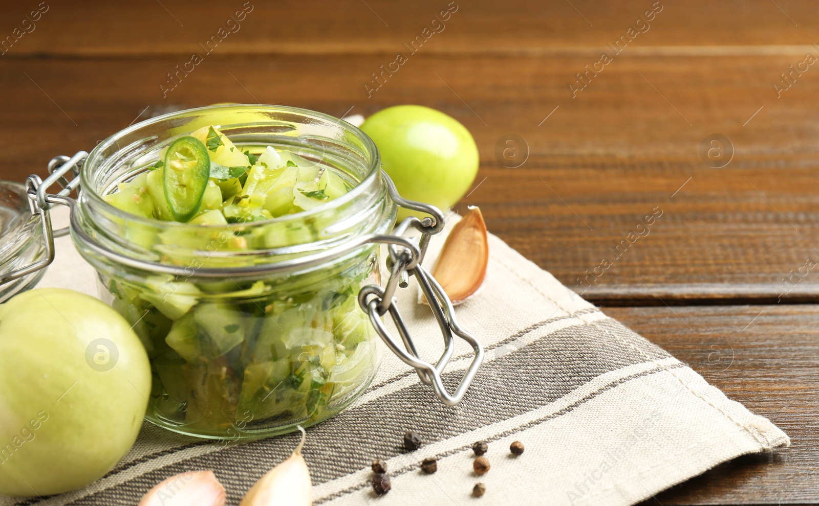 Photo of Delicious green salsa in jar and ingredients on wooden table, closeup. Space for text