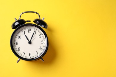 Photo of Black alarm clock on yellow background, top view. Space for text