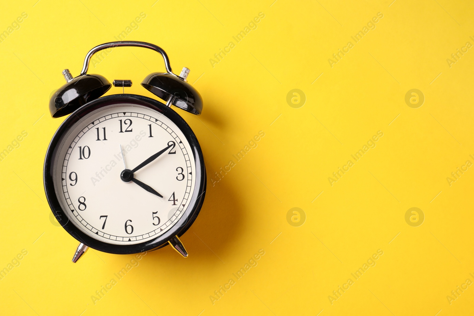 Black alarm clock on yellow background, top view. Space for text Photo of Black alarm clock on yellow background, top view. Space for text