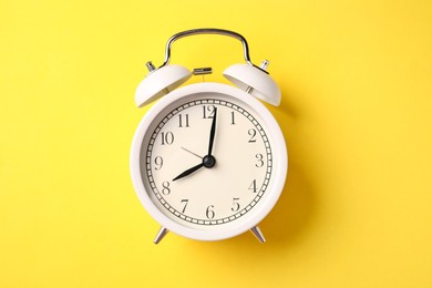Photo of White alarm clock on yellow background, top view