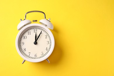 Photo of White alarm clock on yellow background, top view. Space for text