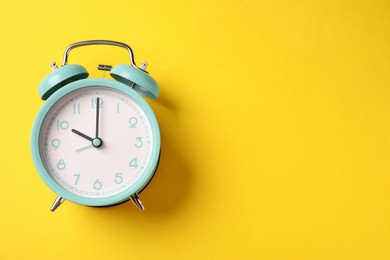 Photo of Turquoise alarm clock on yellow background, top view. Space for text