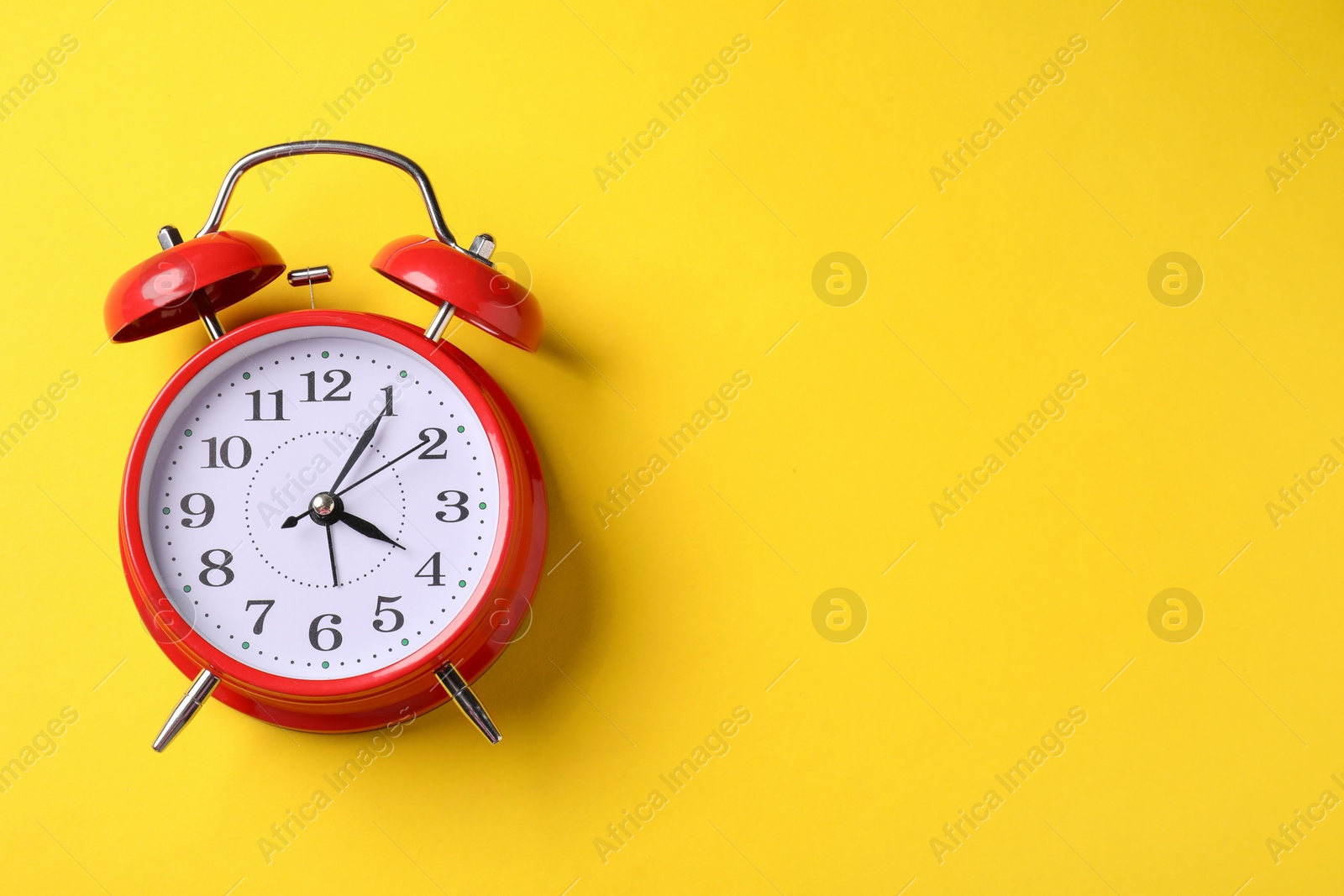 Red alarm clock on yellow background, top view. Space for text Photo of Red alarm clock on yellow background, top view. Space for text