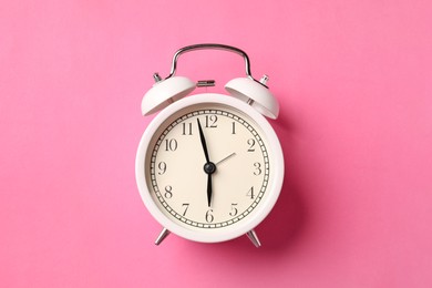 Photo of White alarm clock on pink background, top view