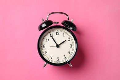 Photo of Black alarm clock on pink background, top view