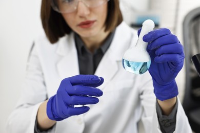 Photo of Scientist holding flask with sample in laboratory, closeup