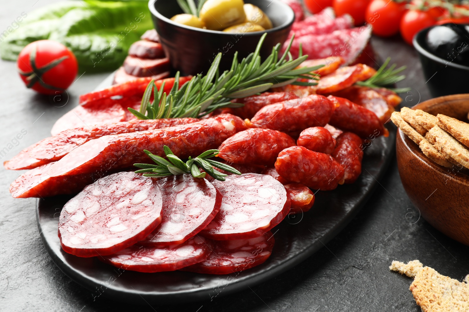 Photo of Different smoked sausages and other snacks on black table, closeup