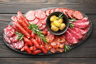 Photo of Different smoked sausages, olives and rosemary on wooden table, top view