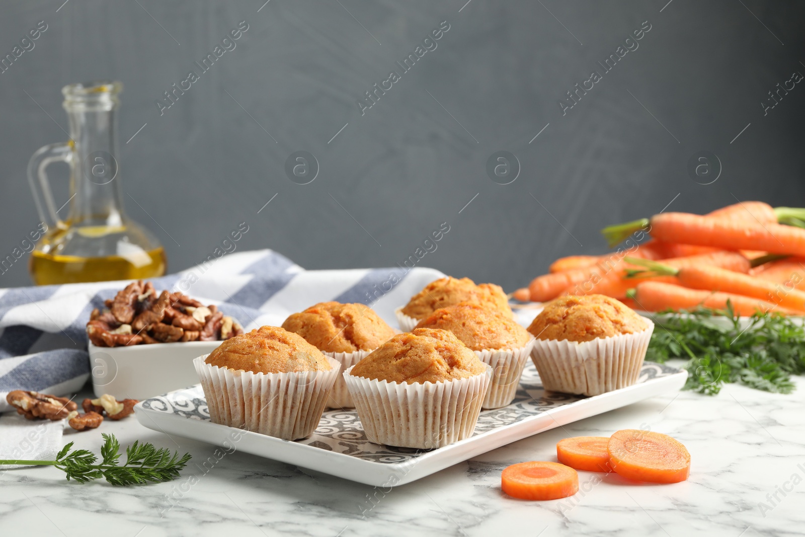 Photo of Tasty carrot muffins, fresh vegetables and walnuts on white marble table, closeup