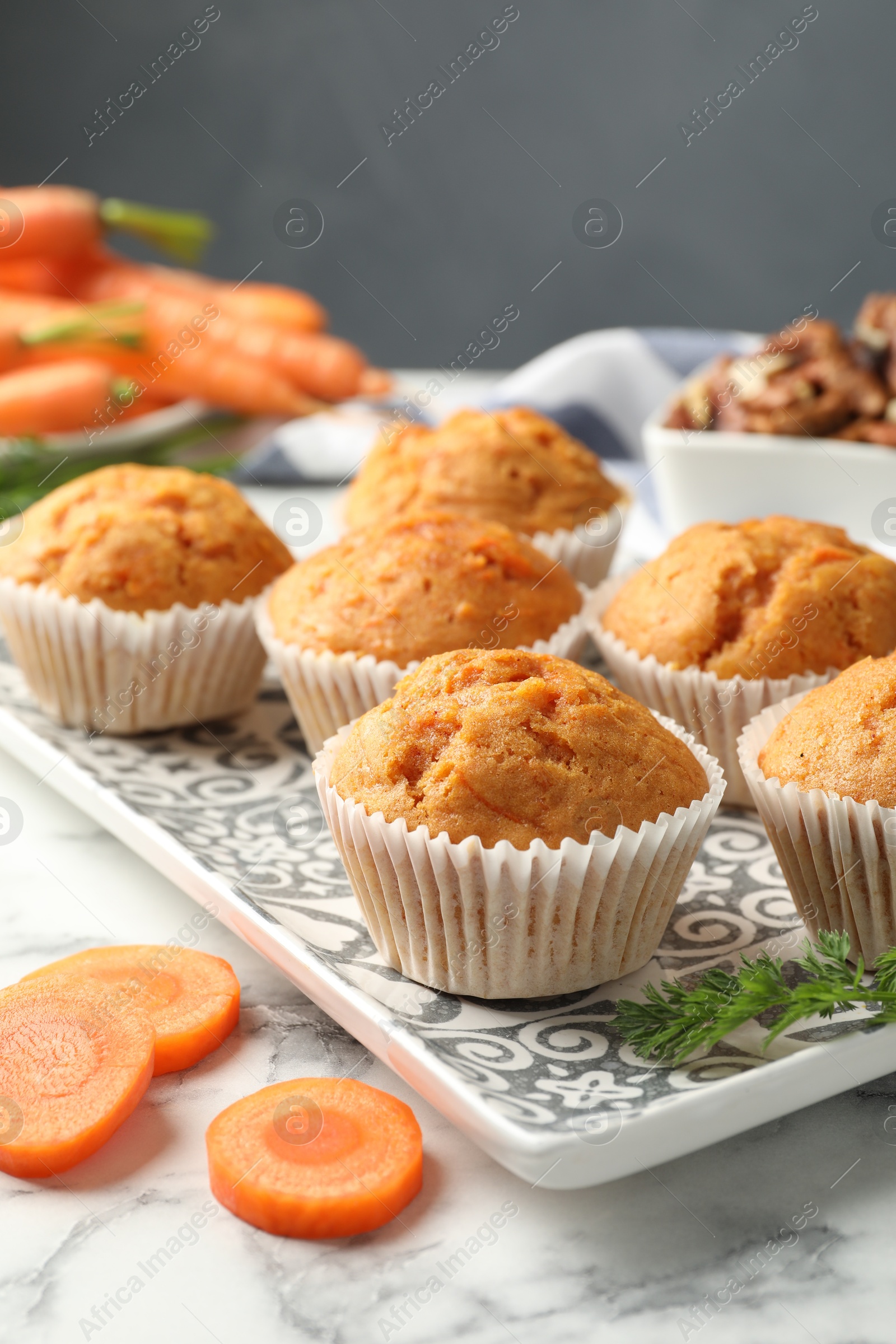 Photo of Tasty carrot muffins, fresh vegetables and walnuts on white marble table, closeup