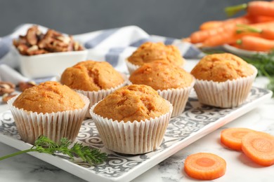 Photo of Tasty carrot muffins, fresh vegetables and walnuts on white marble table, closeup