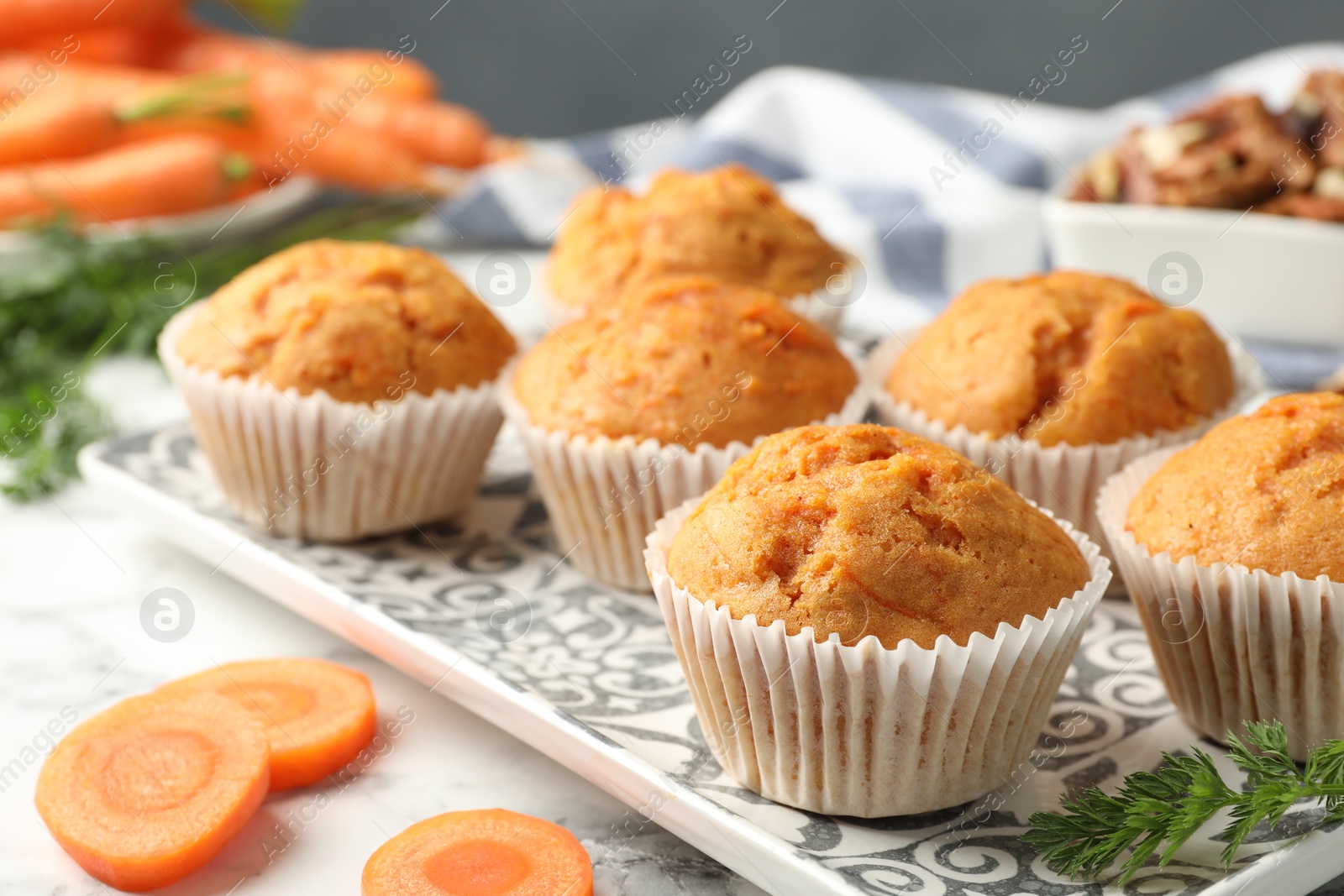 Photo of Tasty carrot muffins and fresh vegetables on white marble table, closeup