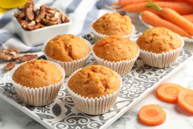 Photo of Tasty carrot muffins, fresh vegetables and walnuts on white marble table, closeup