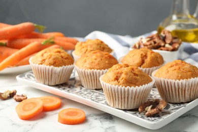 Photo of Tasty carrot muffins, fresh vegetables and walnuts on white marble table, closeup