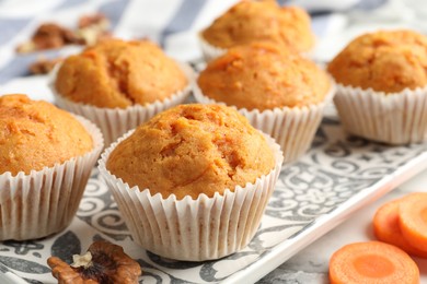 Photo of Tasty carrot muffins and cut vegetable on white marble table, closeup