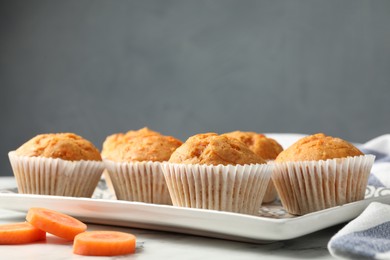 Photo of Tasty carrot muffins and cut vegetable on white marble table, closeup