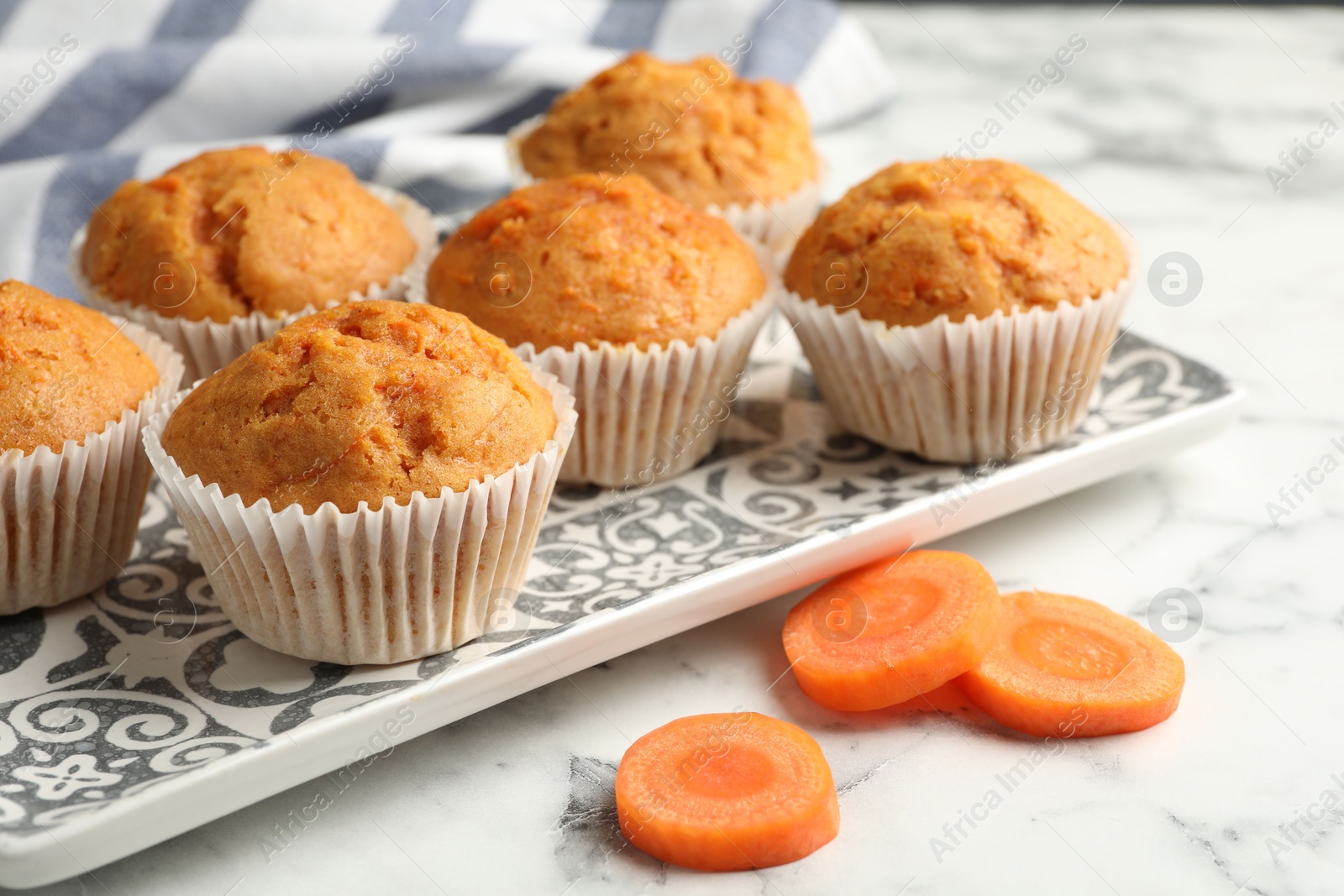 Photo of Tasty carrot muffins and cut vegetable on white marble table, closeup