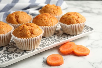 Photo of Tasty carrot muffins and cut vegetable on white marble table, closeup