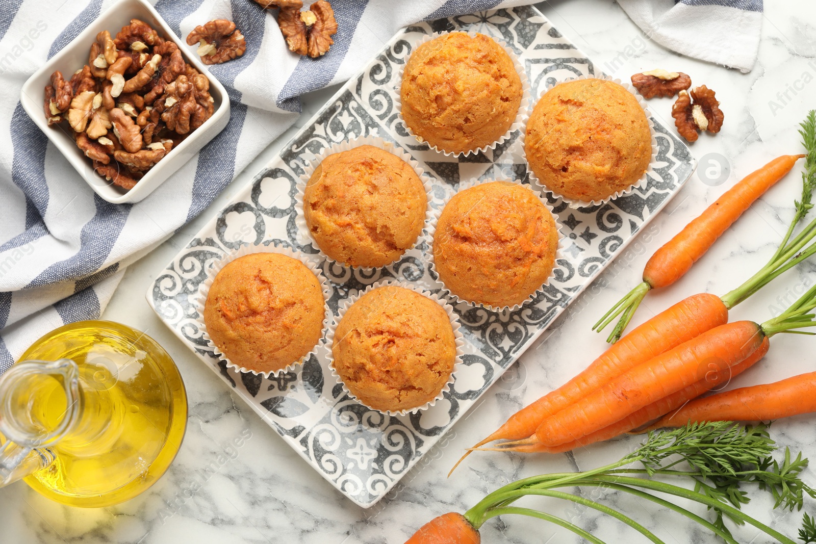 Photo of Tasty carrot muffins, fresh vegetables and walnuts on white marble table, flat lay