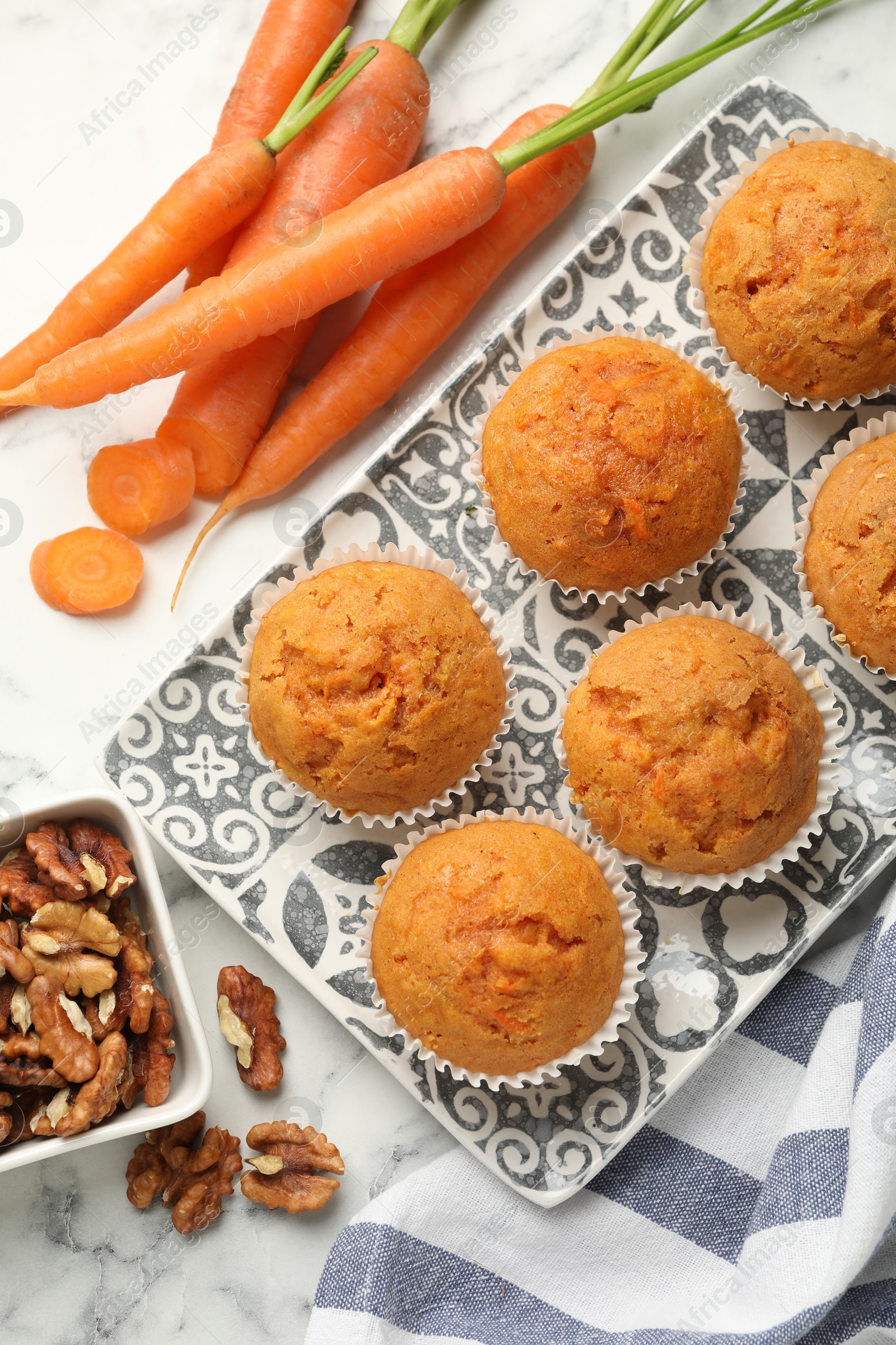 Photo of Tasty carrot muffins, fresh vegetables and walnuts on white marble table, flat lay