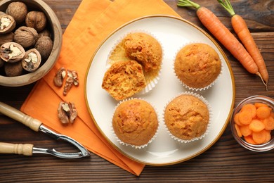 Photo of Tasty carrot muffins, fresh vegetables, nutcracker and walnuts on wooden table, flat lay