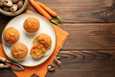 Photo of Tasty carrot muffins, fresh vegetables, nutcracker and walnuts on wooden table, flat lay. Space for text