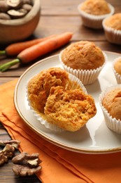 Photo of Tasty carrot muffins, fresh vegetables and walnuts on wooden table, closeup