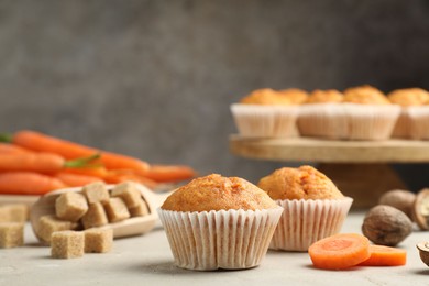 Photo of Tasty carrot muffins, fresh vegetables, sugar and walnuts on light grey table, closeup