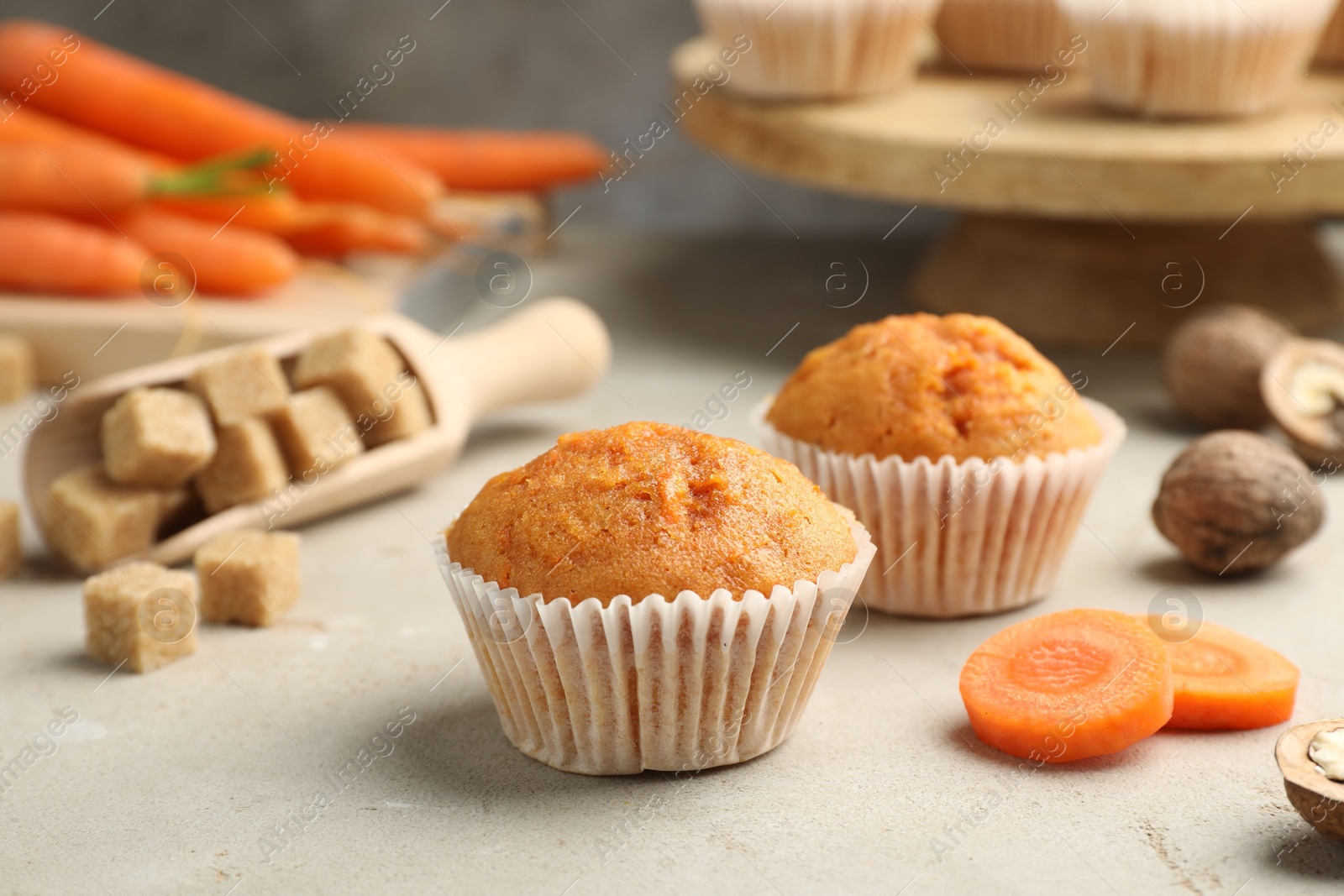 Photo of Tasty carrot muffins, fresh vegetables, sugar and walnuts on light grey table, closeup