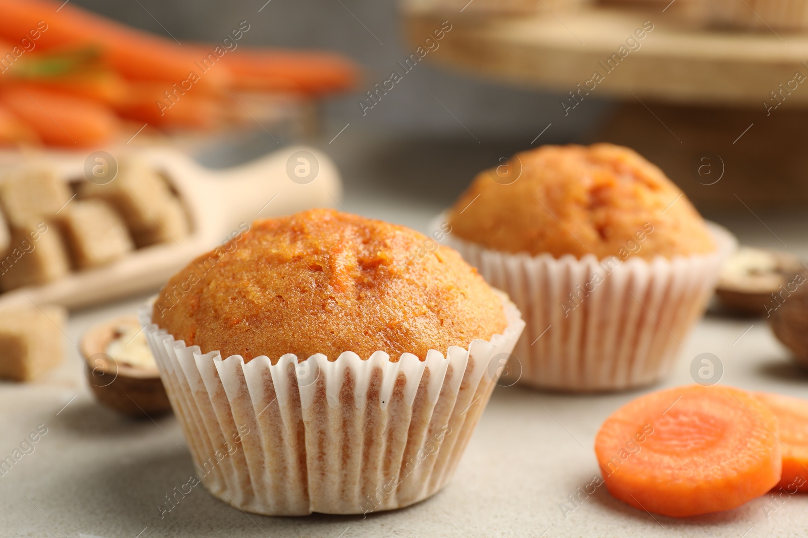 Photo of Tasty carrot muffins and cut vegetable on light grey table, closeup