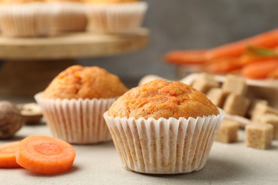 Photo of Tasty carrot muffins and cut vegetable on light grey table, closeup