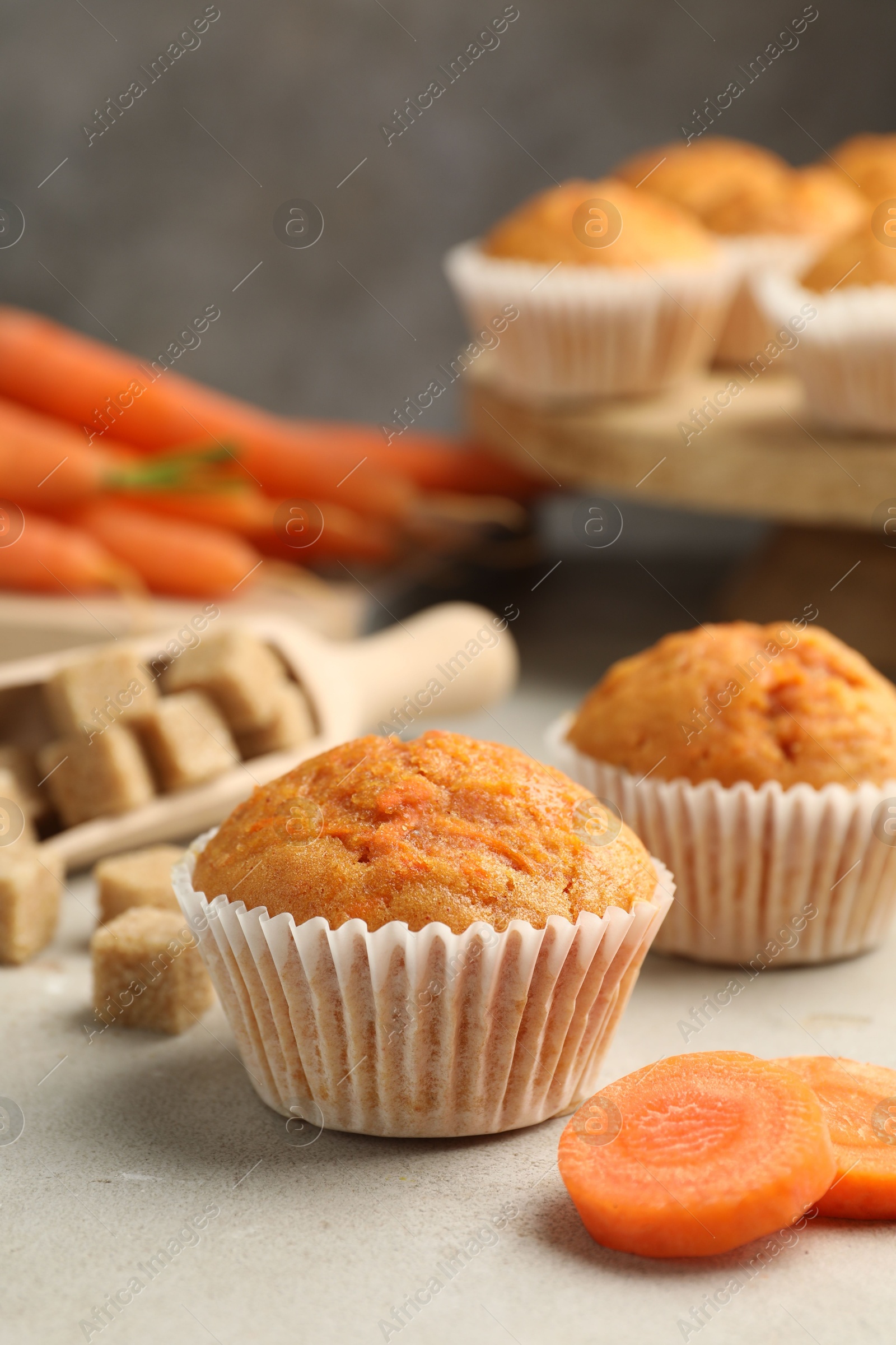 Photo of Tasty carrot muffins, sugar and fresh vegetables on light grey table, closeup