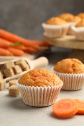 Photo of Tasty carrot muffins, sugar and fresh vegetables on light grey table, closeup