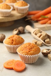 Photo of Tasty carrot muffins, fresh vegetables, sugar and walnuts on light grey table, closeup