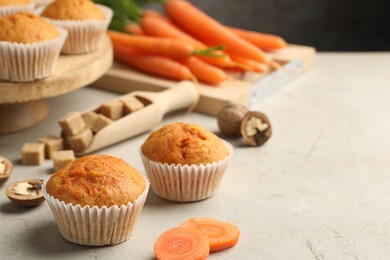 Photo of Tasty carrot muffins, fresh vegetables, sugar and walnuts on light grey table, closeup. Space for text