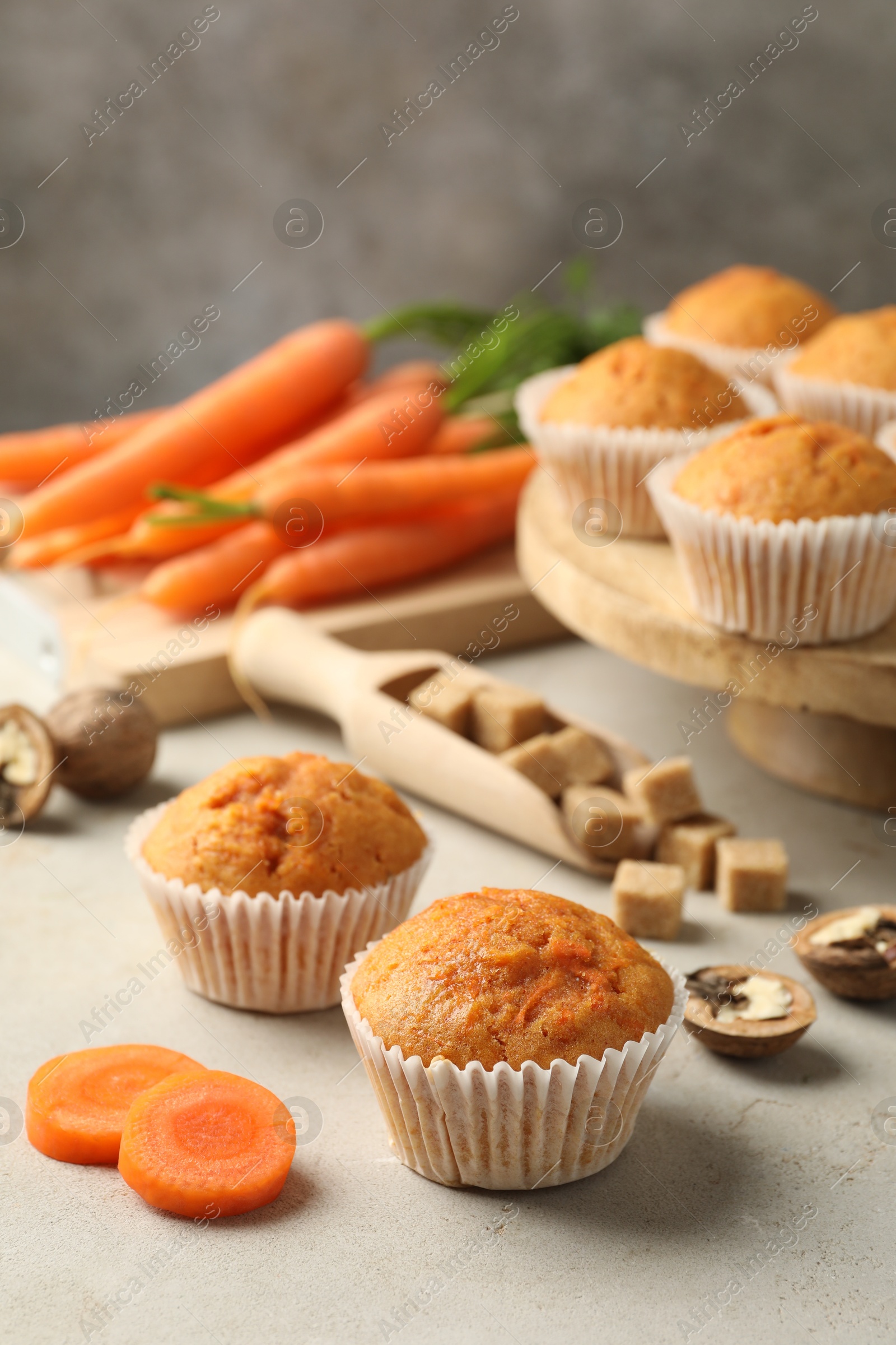 Photo of Tasty carrot muffins, fresh vegetables, sugar and walnuts on light grey table, closeup