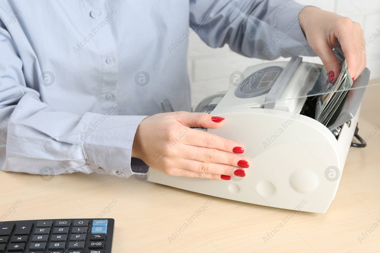 Photo of Cashier using money counting machine at table in currency exchange, closeup