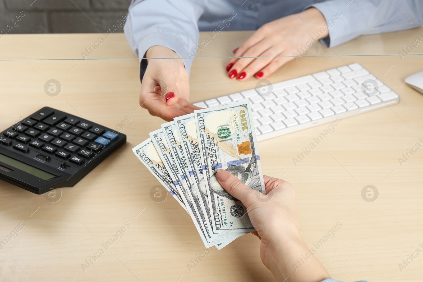 Photo of Client giving dollar banknotes to cashier at table in money exchange, closeup