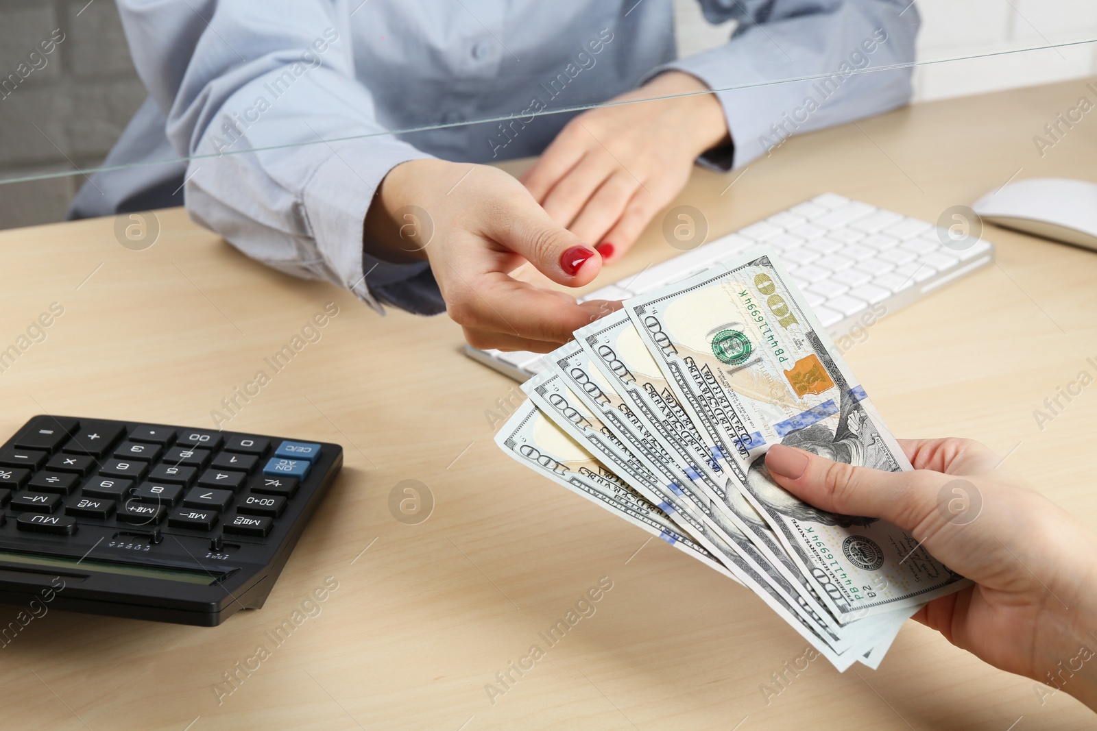 Photo of Client giving dollar banknotes to cashier at table in money exchange, closeup