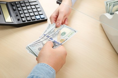 Photo of Client giving dollar banknotes to cashier at table in money exchange, closeup