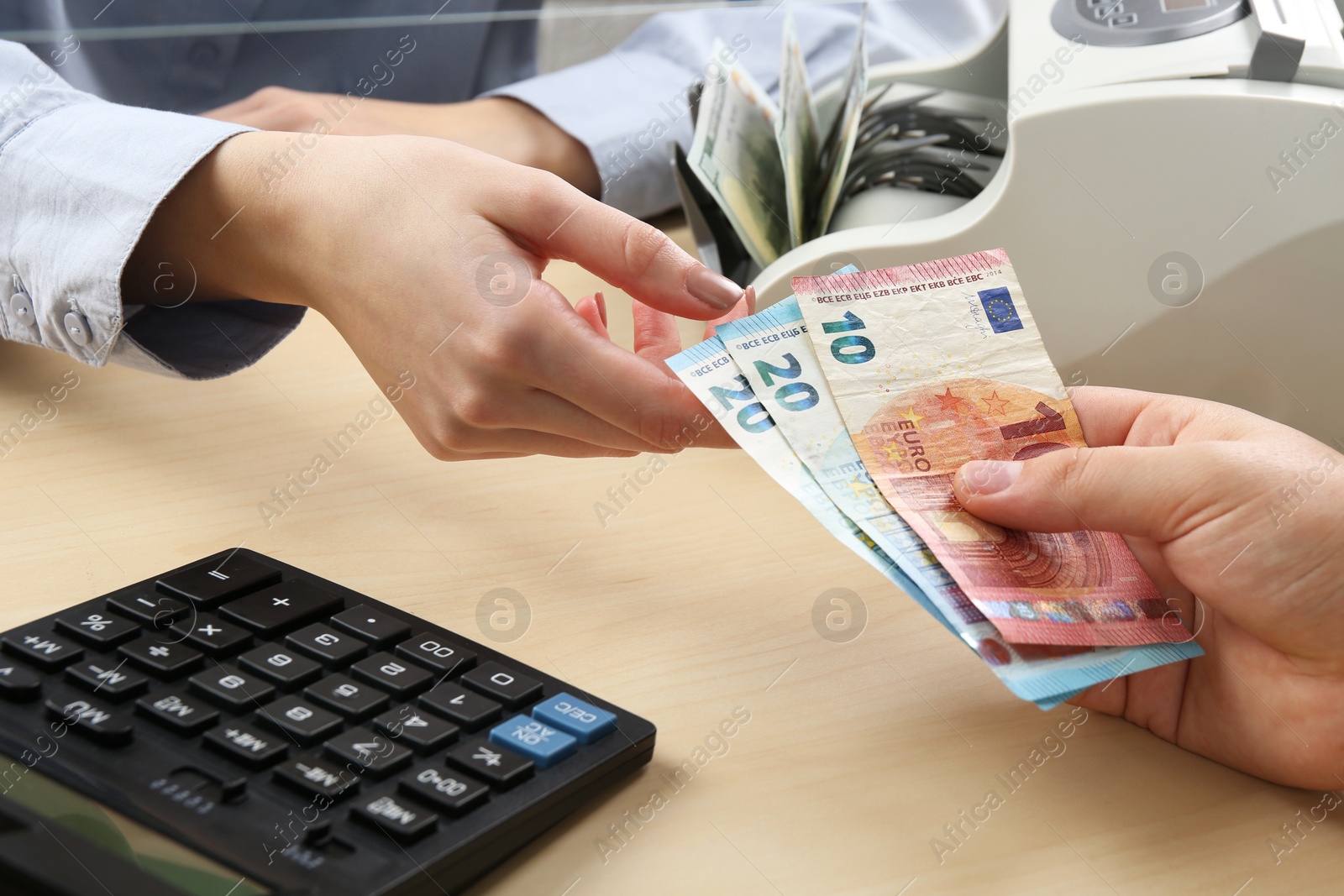 Photo of Client giving euro banknotes to cashier at table in money exchange, closeup